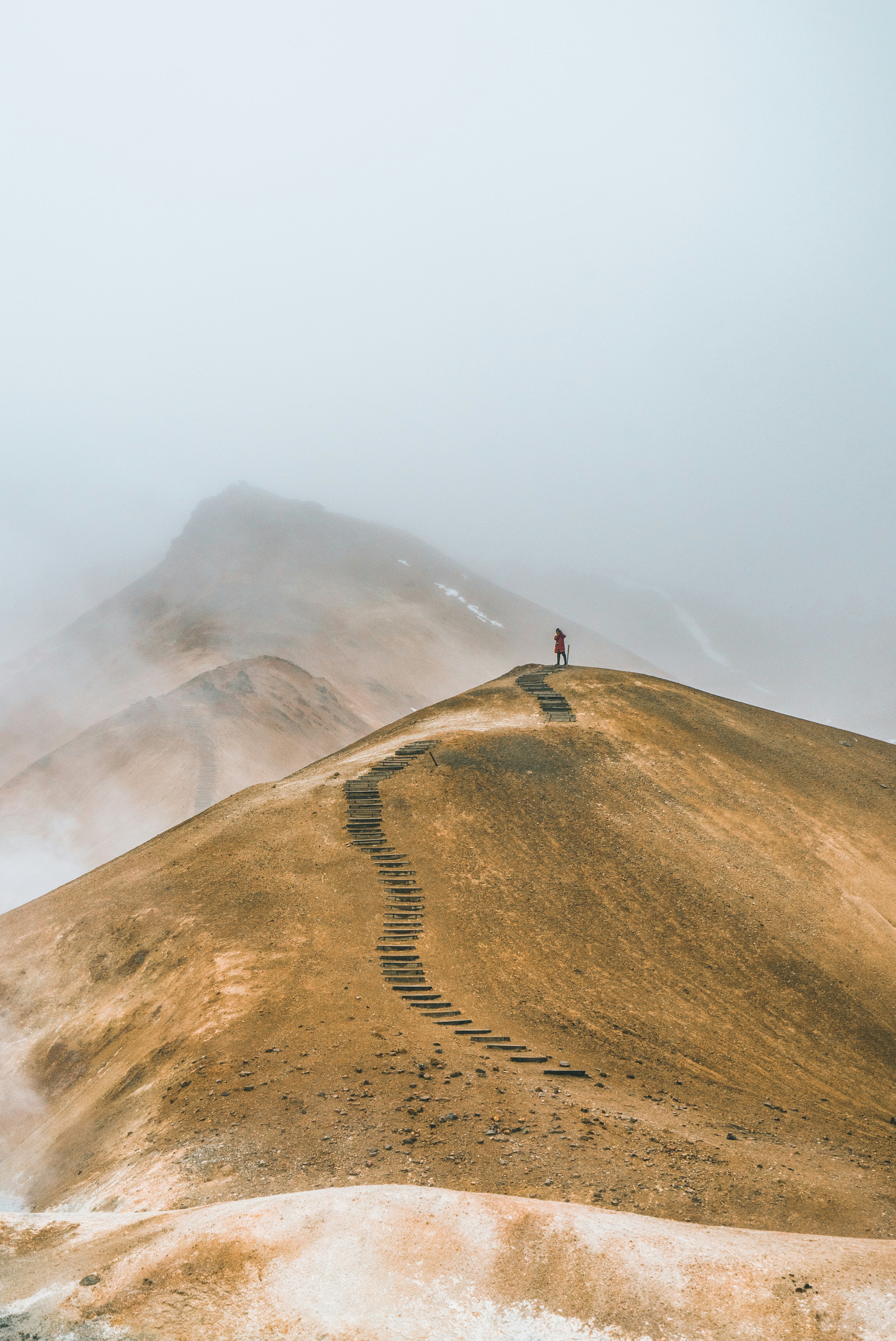 Icelandic photo of a man at the top of Brown Hill, with cloudy sky and a misty mountain landscape in the background